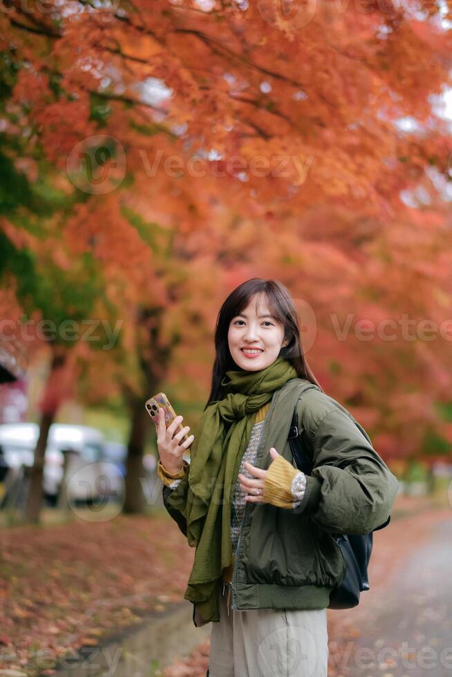 Asian woman enjoys the fall outdoors, adorned in a fashionable sweater. A pretty and cheerful portrait amid nature's vibrant colors. photo