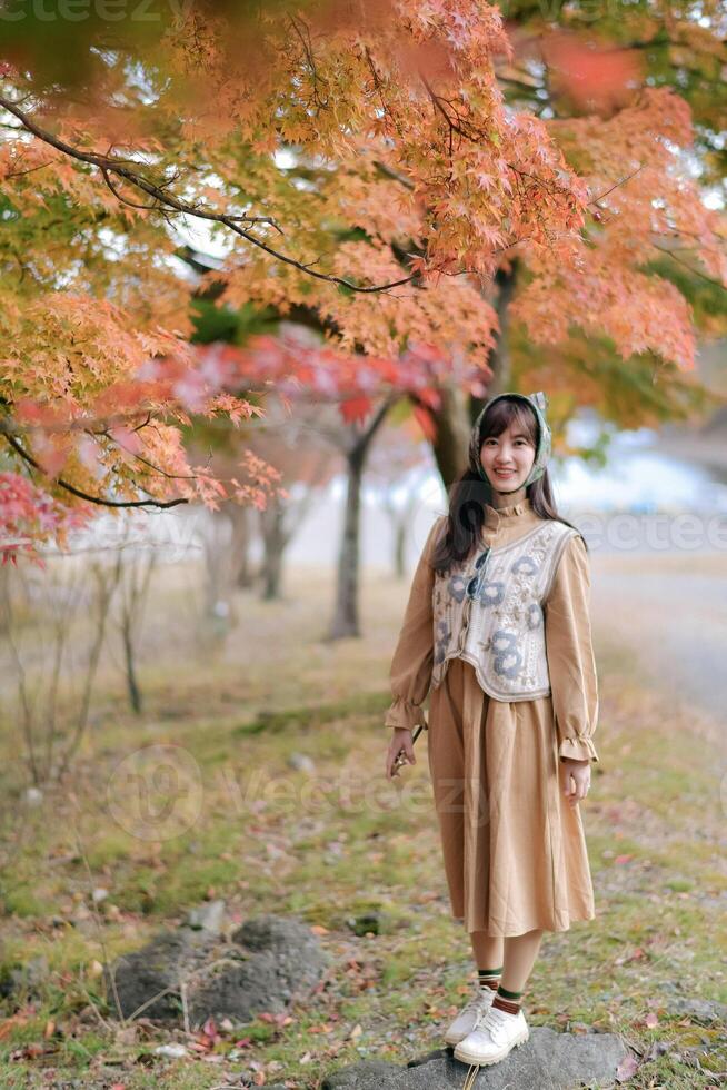 Asian woman in casual dress enjoys Japan's beauty, walking amid vibrant foliage. A cheerful holiday portrait capturing the essence of nature, fashion, and a journey. photo
