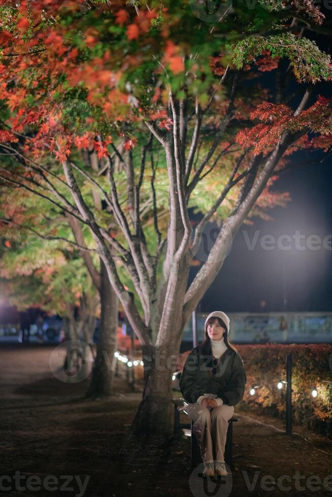 Asian woman, adorned in a chic jacket, experiences the holiday magic in Kawaguchiko. A festive night filled with joy and snowy delight. photo
