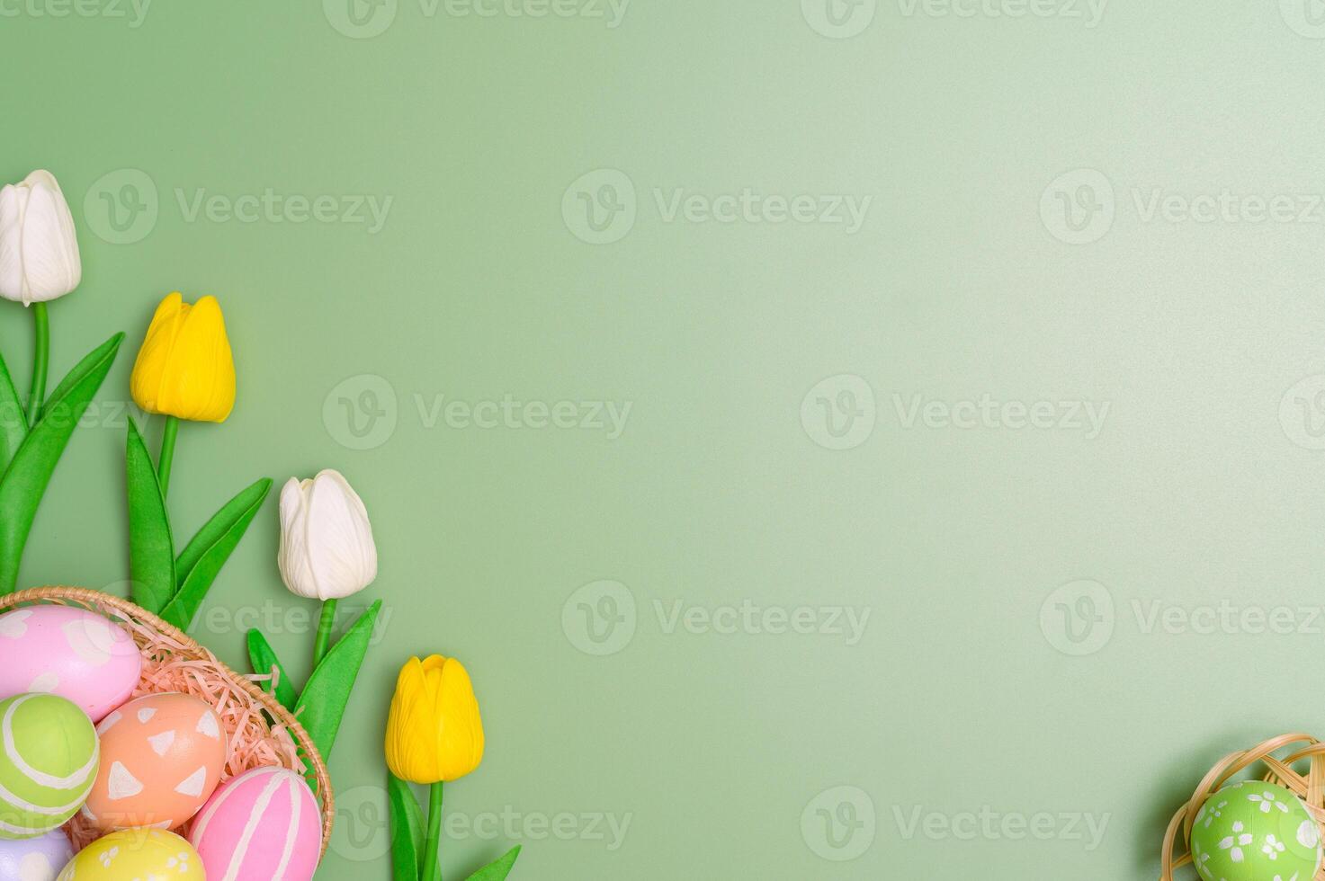 Happy Easter holiday greeting card design concept. Colorful Easter Eggs and spring flowers on pastel green background. Flat lay, top view, copy space. photo