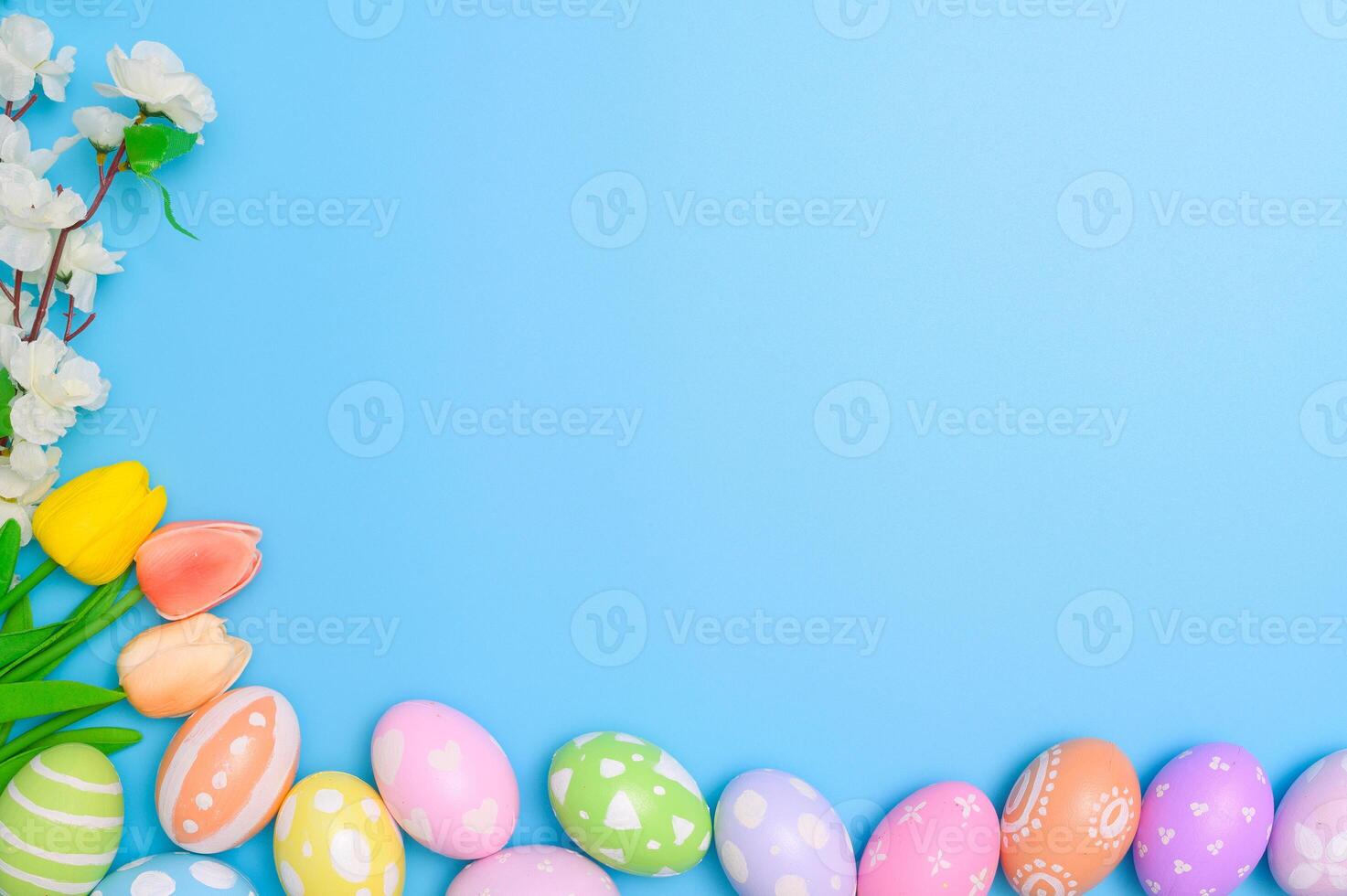 Happy Easter holiday greeting card design concept. Colorful Easter Eggs and spring flowers on blue background. Flat lay, top view, copy space. photo