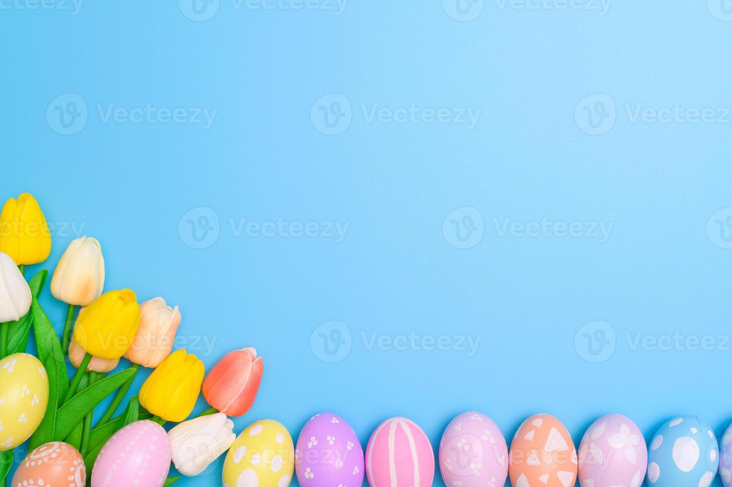 Happy Easter holiday greeting card design concept. Colorful Easter Eggs and spring flowers on blue background. Flat lay, top view, copy space. photo