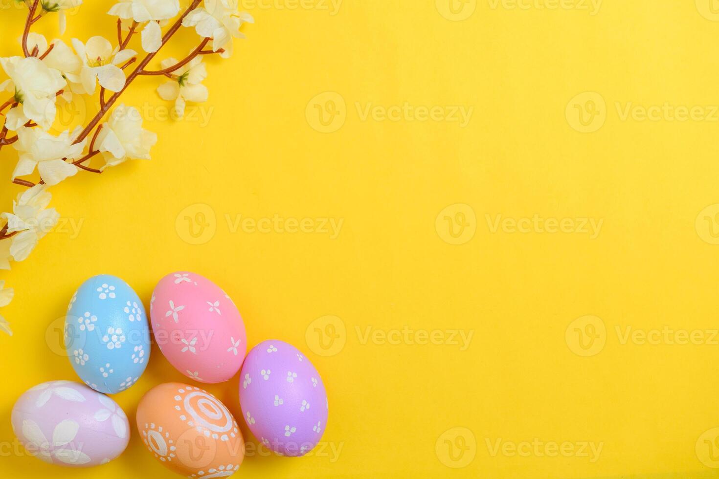 Happy Easter holiday greeting card design concept. Colorful Easter Eggs and spring flowers on yellow background. Flat lay, top view, copy space. photo