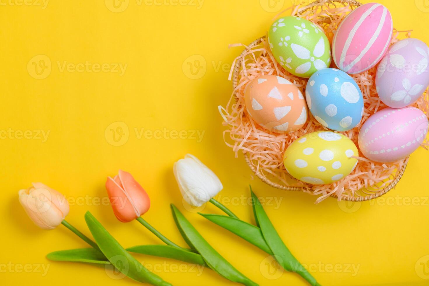 Happy Easter holiday greeting card design concept. Colorful Easter Eggs and spring flowers on yellow background. Flat lay, top view, copy space. photo