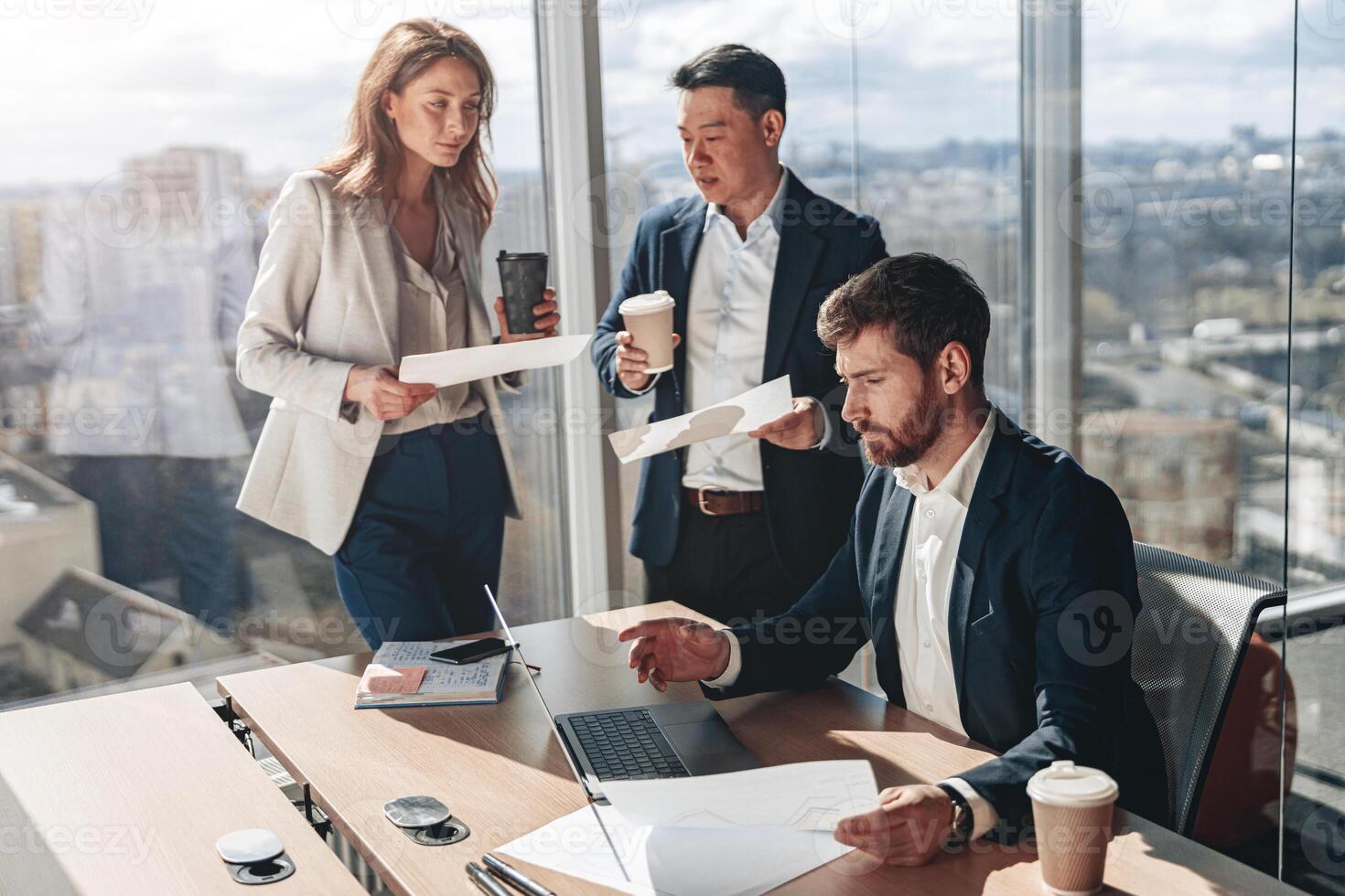 Focused businessmen drink coffee and discussing documents with graphs and charts in a modern office photo