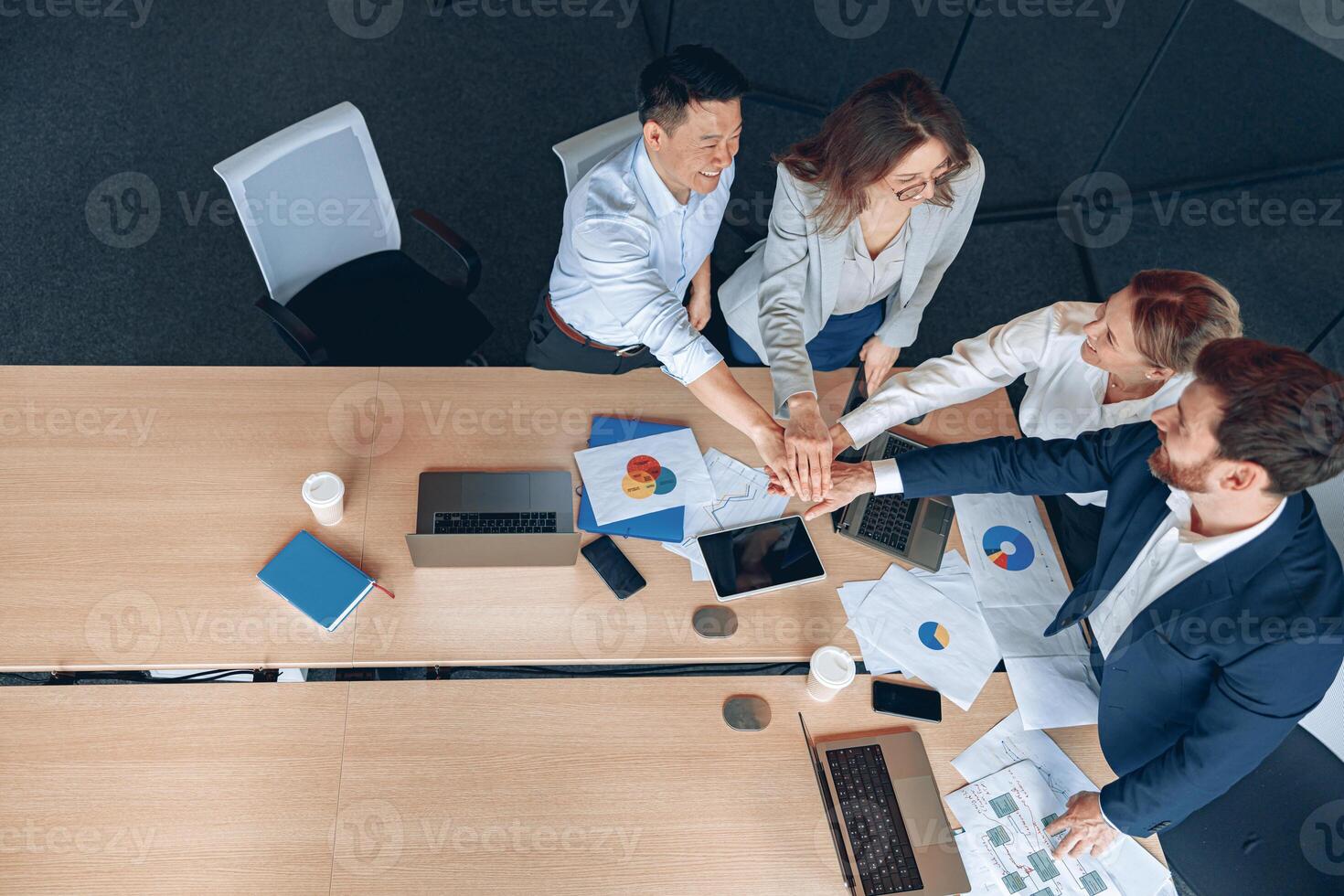 Diverse business people group put hands together while standing near the table in office photo