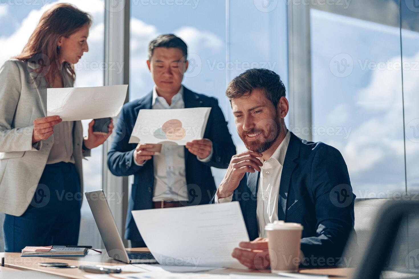Focused businessmen discussing work issues using laptop and documents with charts in a modern office photo