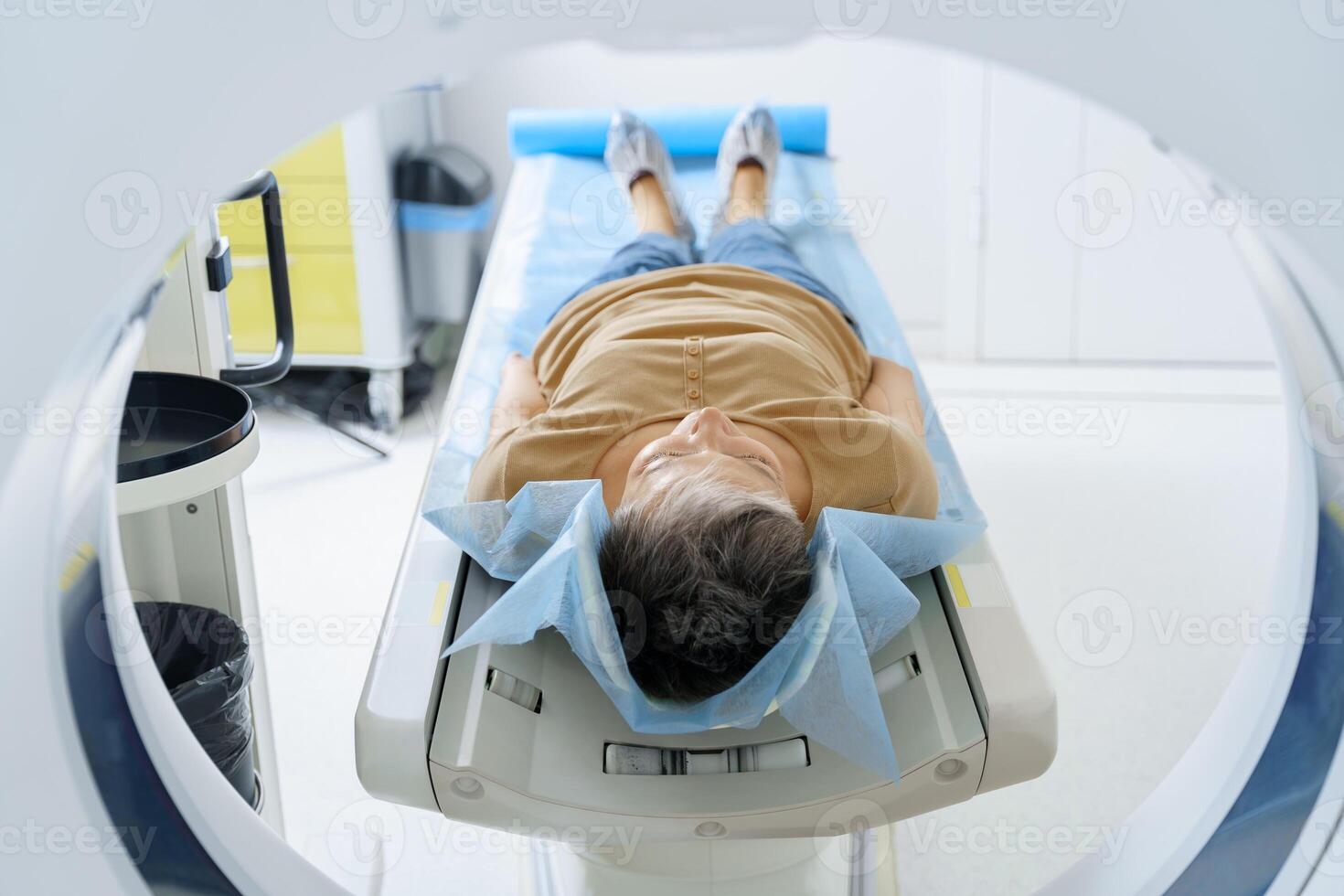 Female patient lying on table and entering CT machine during examination procedure in hospital photo