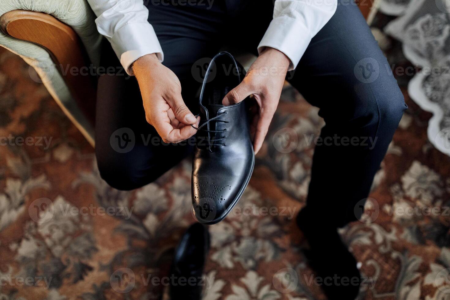 A man is sitting on a chair and holding a black shoe photo
