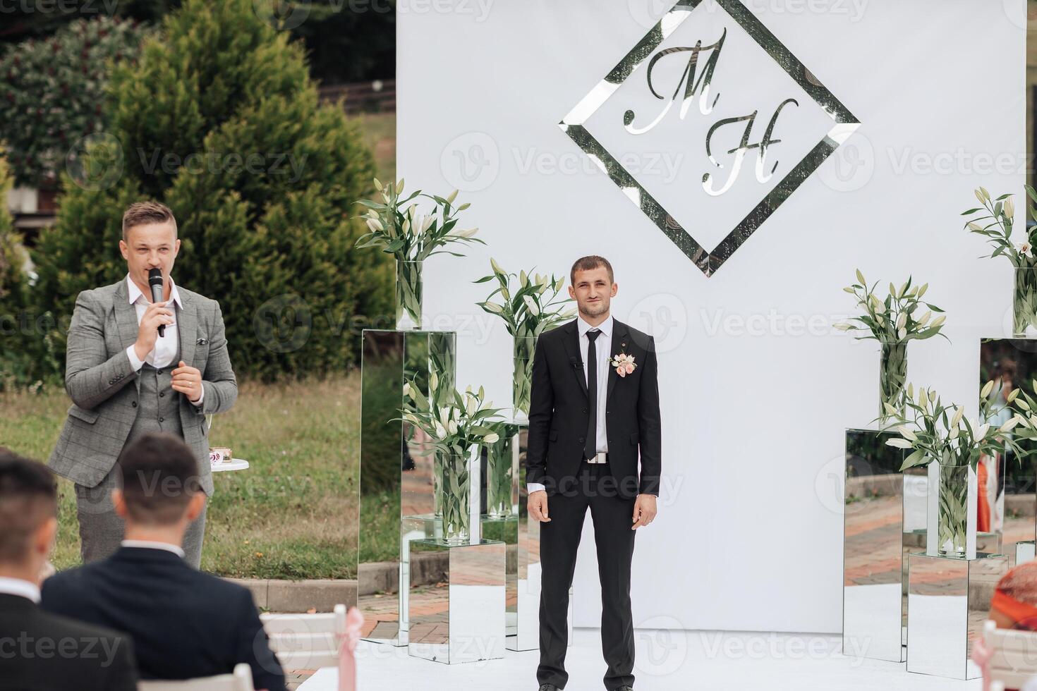 A man stands in front of a white wall with the letters M and H on it photo