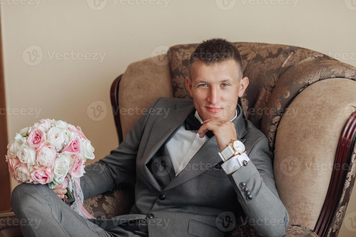 A man in a suit and tie sits in a chair with a bouquet of flowers in his lap photo