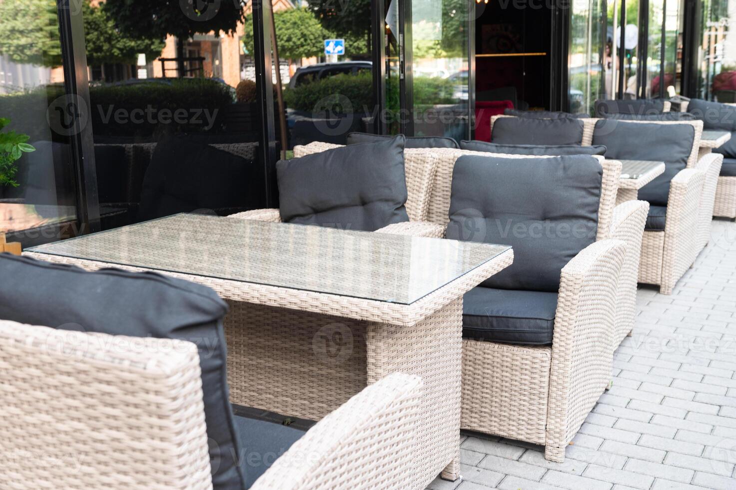 Outdoor cafe seating with wicker furniture and glass table in front of large windows photo