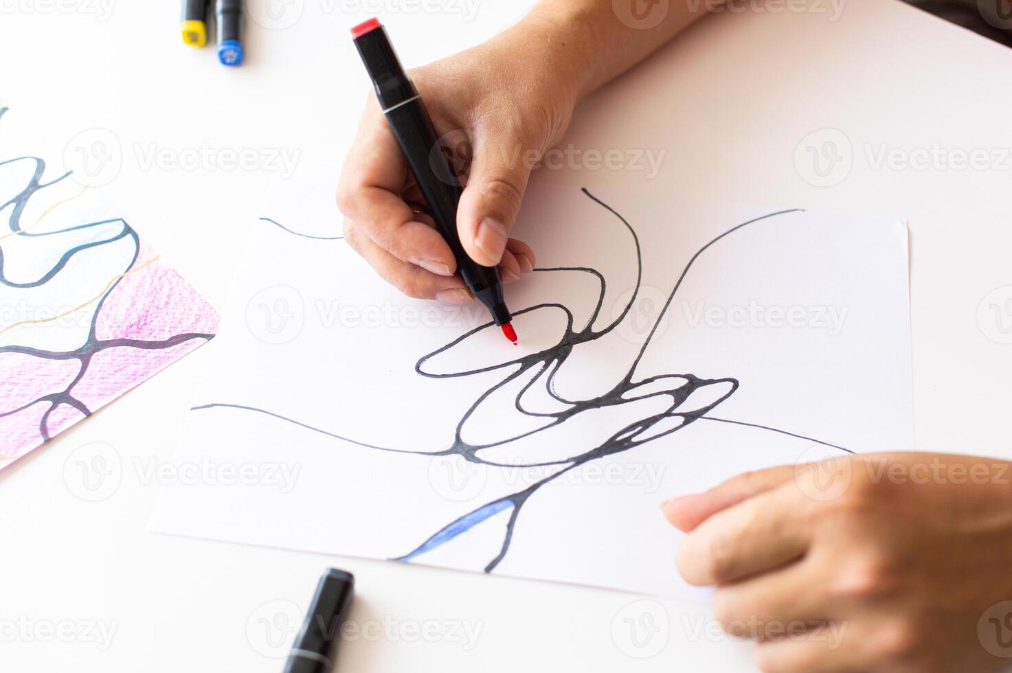Hands drawing abstract lines with a black marker on white paper photo