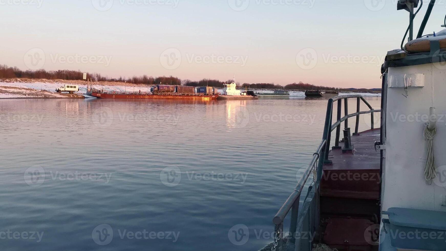 Boat floats on background of river cargo berth. Clip. View from floating boat to shore with pier. Boat sails to shore with barge on sunny winter day photo