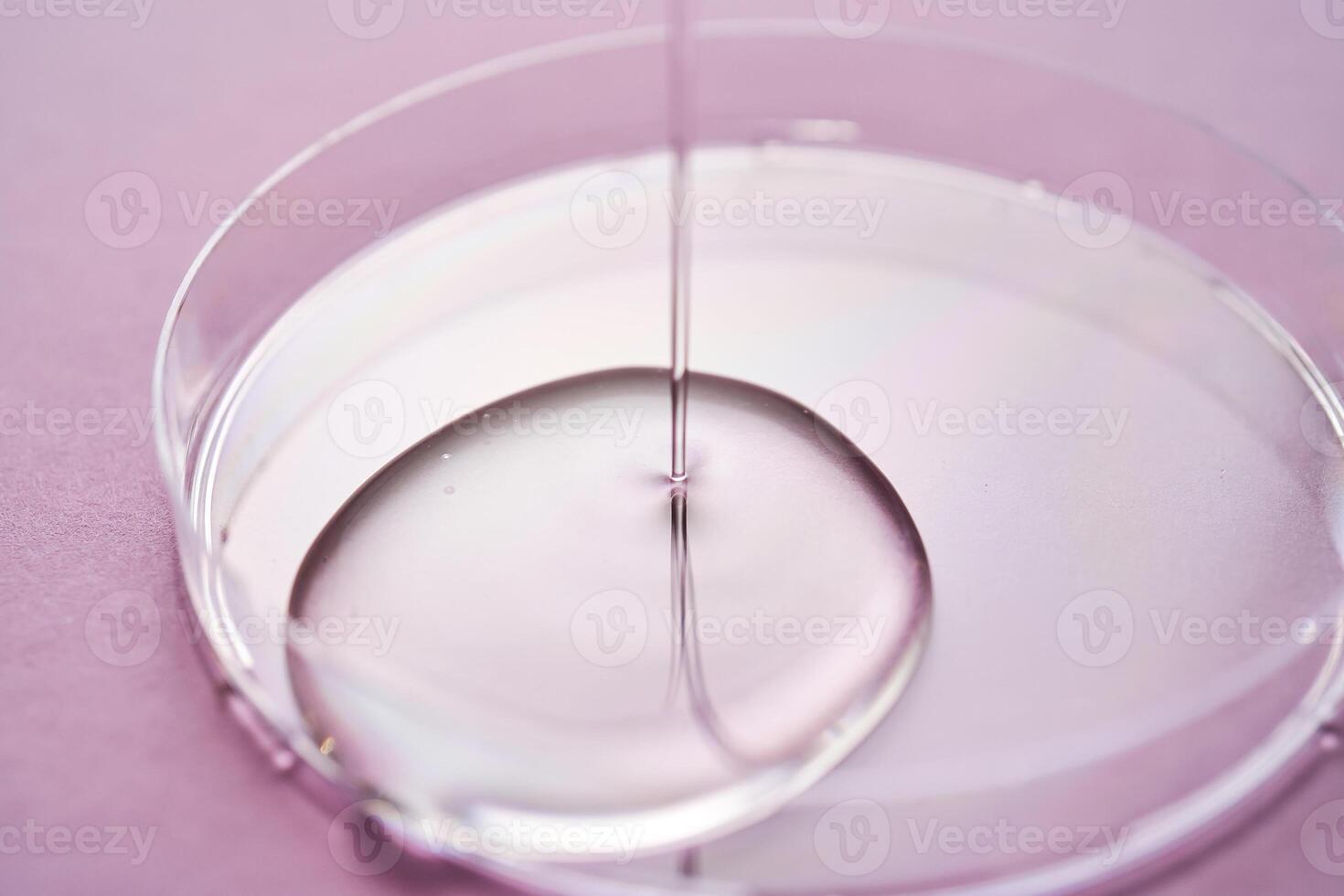 Serum or cosmetic oil flows into a transparent bowl on a purple background. photo