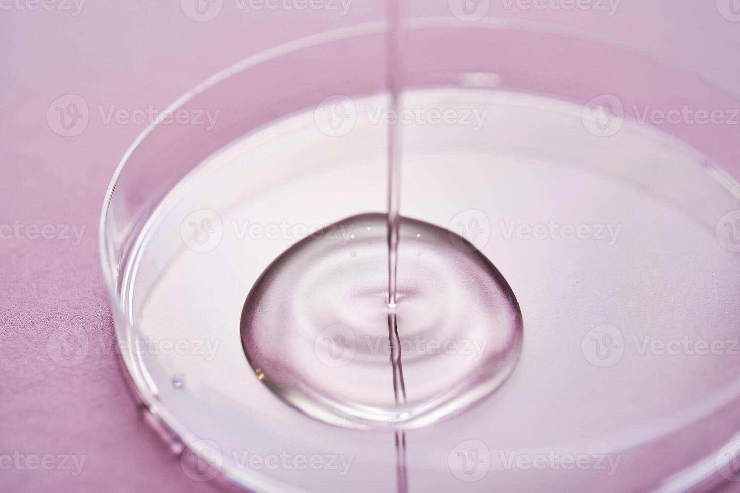 Serum or cosmetic oil flows into a transparent bowl on a purple background. photo