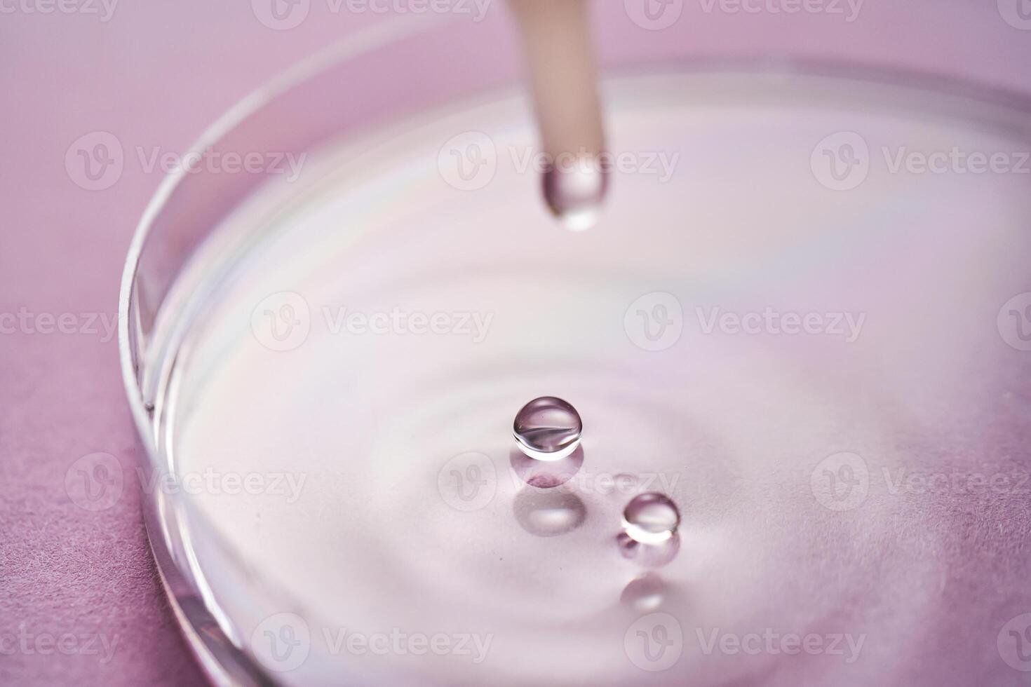 Serum or cosmetic oil flows into a transparent bowl on a purple background. photo