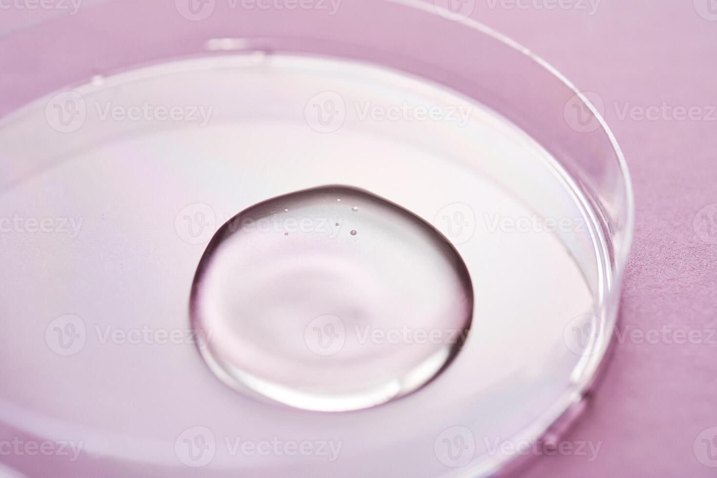 Serum or cosmetic oil flows into a transparent bowl on a purple background. photo