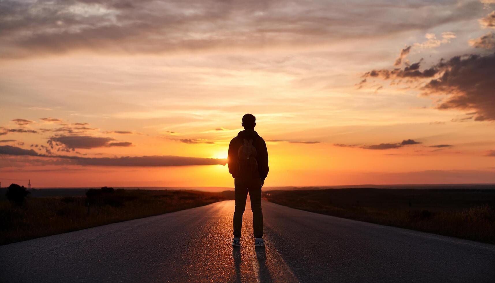 Lonely young man silhouette at sunset, copy space, tourist stand alone by road with epic sky in background. photo