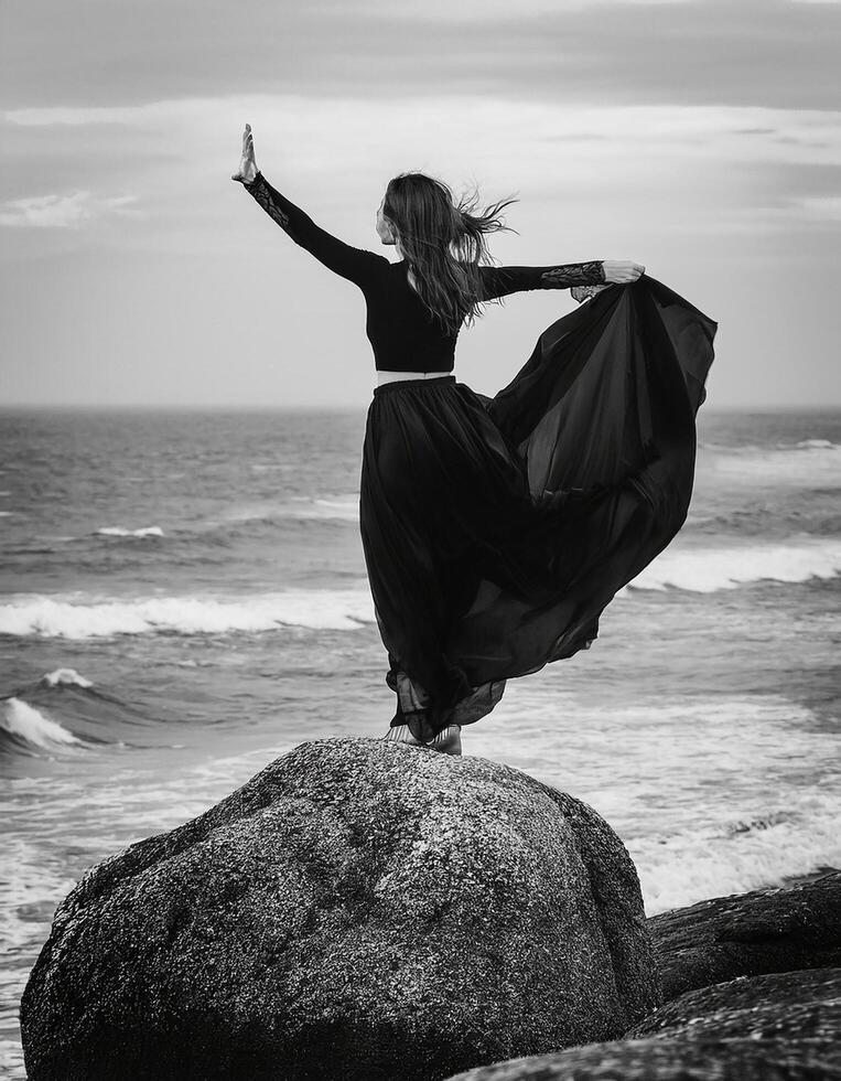 Beautiful lady dancing on the big rock near ocean beach wave with black dress, image in vintage black and white color. photo