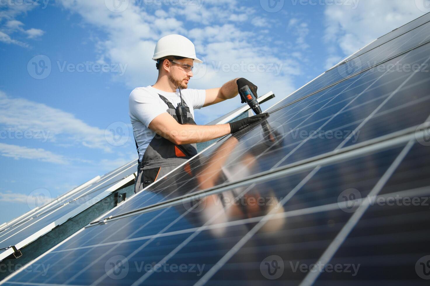 Male worker in uniform with a drill screwdriver in his hand near solar panels photo