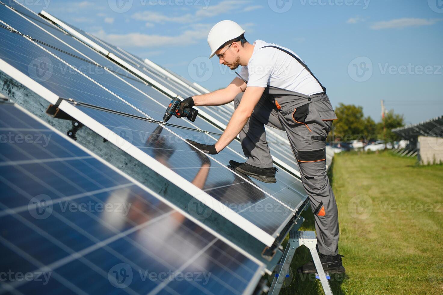 Side view of male worker installing solar modules and support structures of photovoltaic solar array. Electrician wearing safety helmet photo
