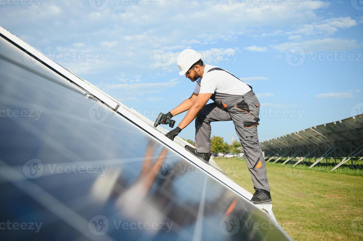 An Indian worker in uniform and with tools works on a solar panel farm photo