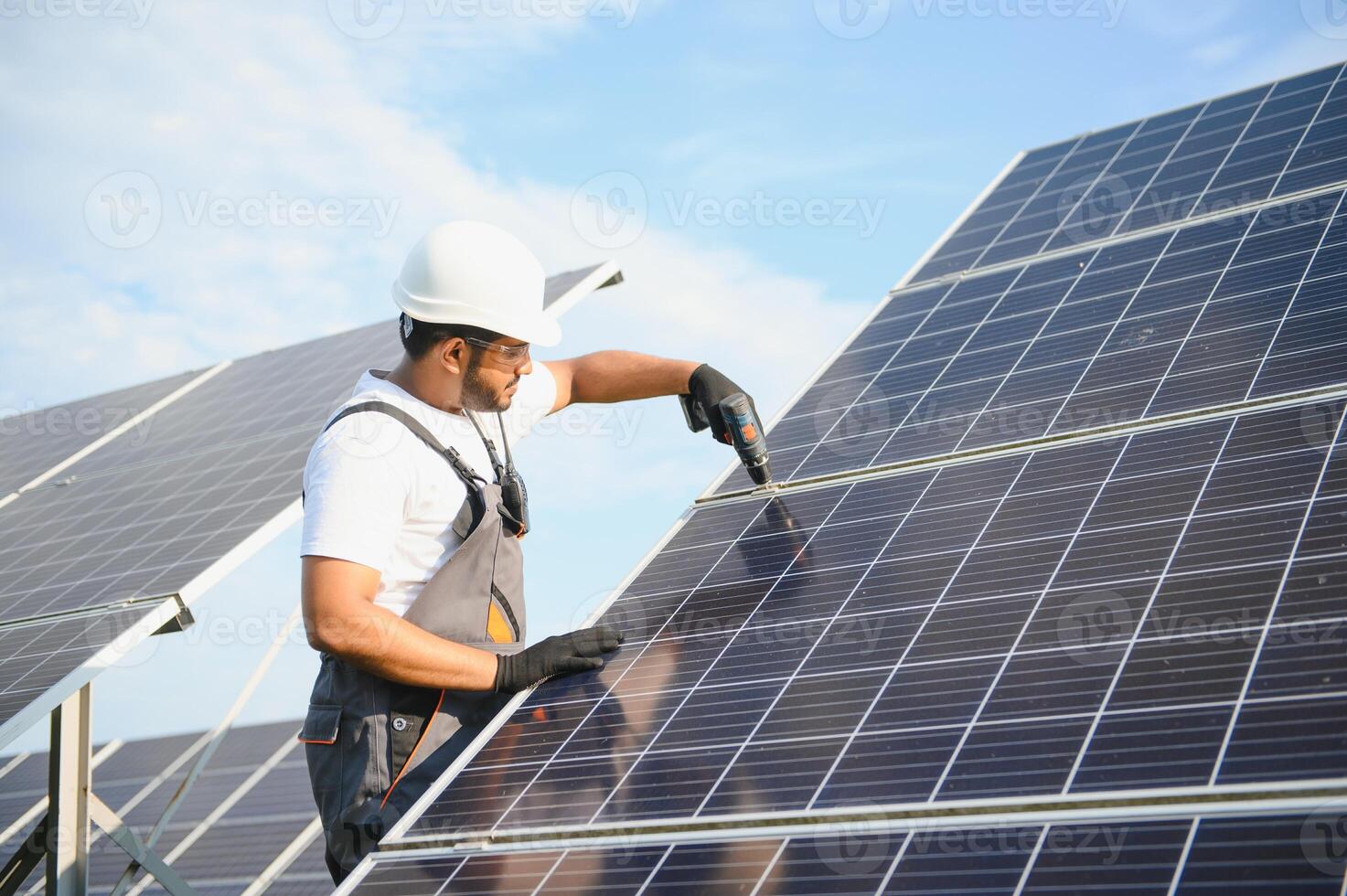An Indian worker in uniform and with tools works on a solar panel farm photo