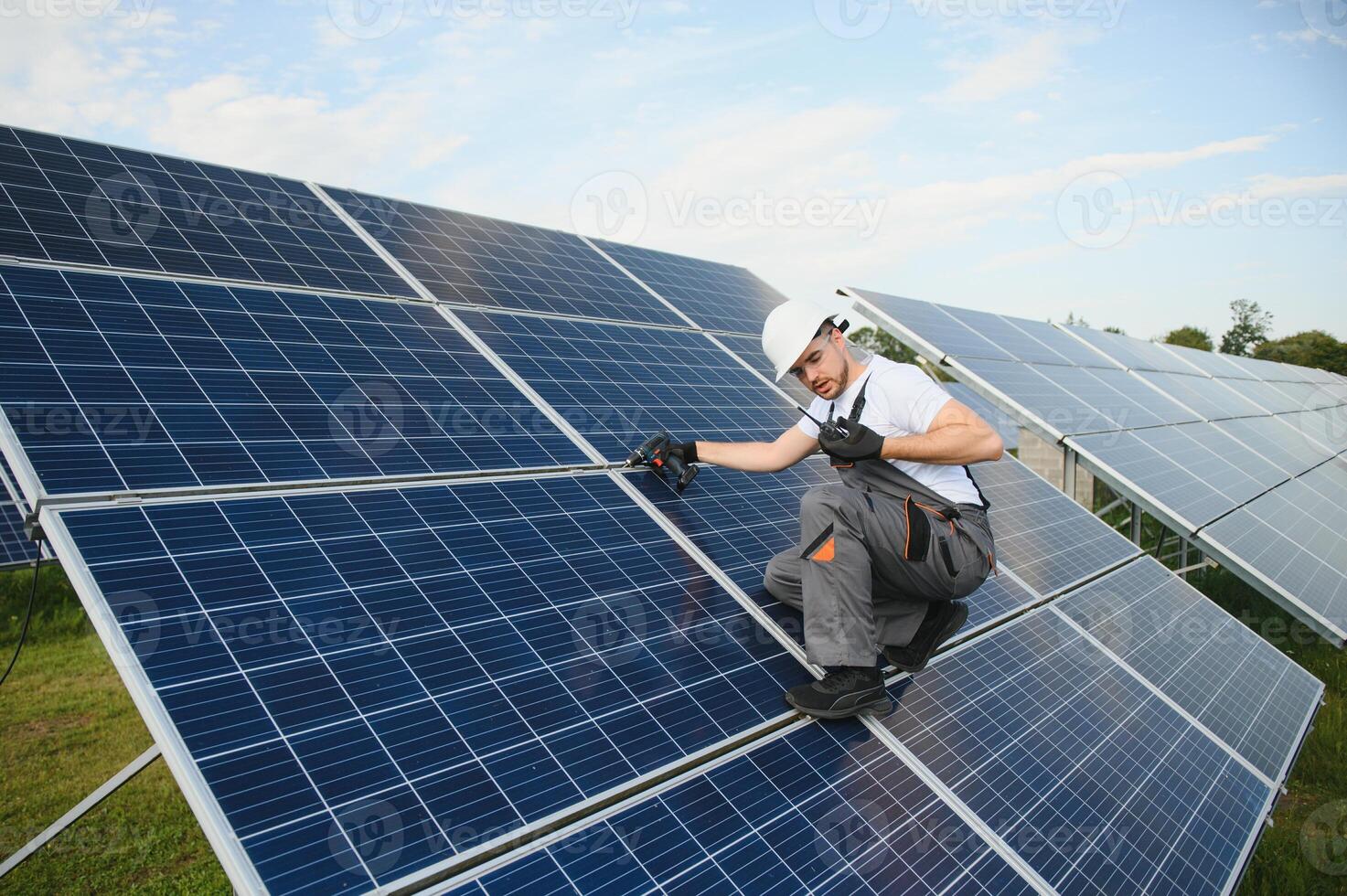 Male worker in uniform with a drill screwdriver in his hand near solar panels photo