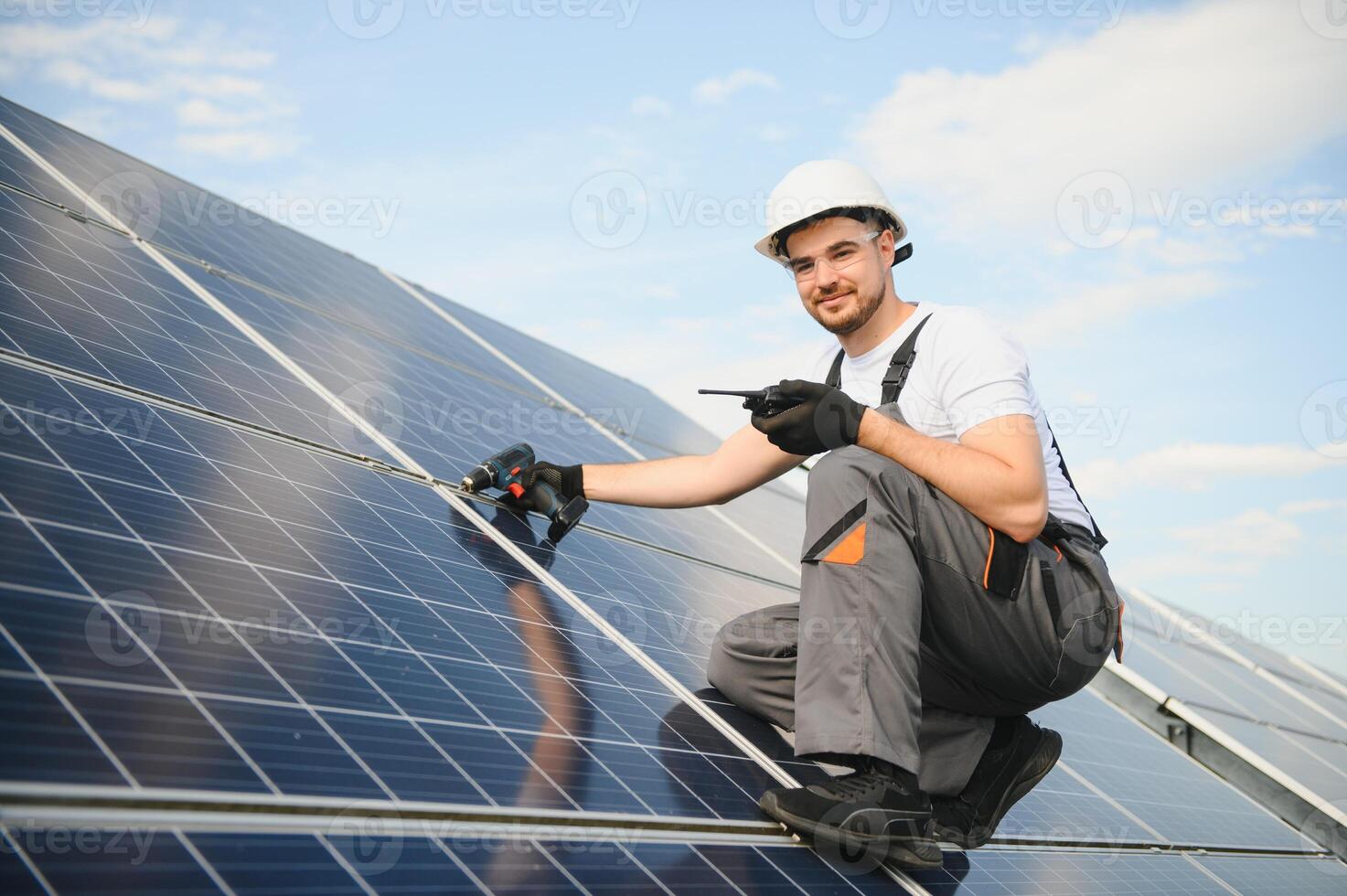 Side view of male worker installing solar modules and support structures of photovoltaic solar array. Electrician wearing safety helmet photo