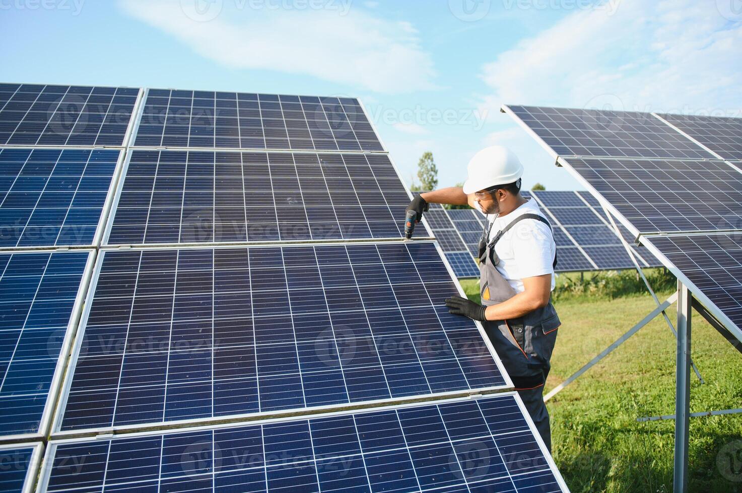 An Indian worker in uniform and with tools works on a solar panel farm photo