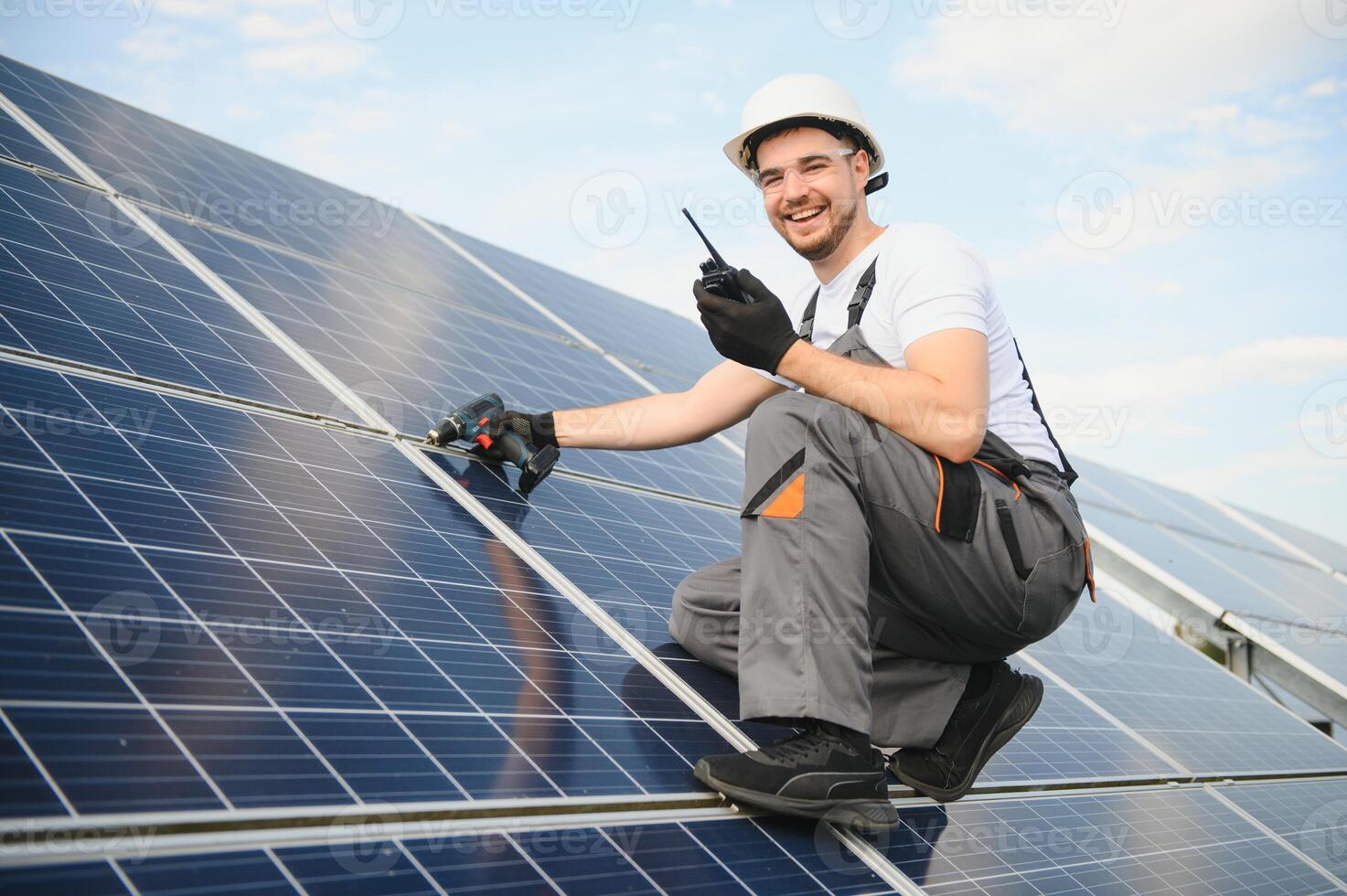 Male worker in uniform with a drill screwdriver in his hand near solar panels photo
