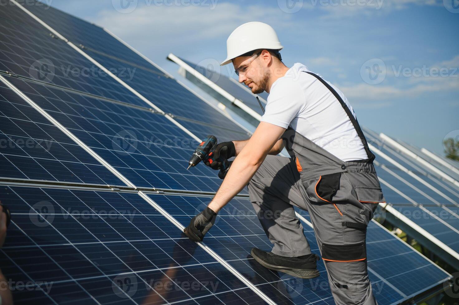 Male worker in uniform with a drill screwdriver in his hand near solar panels photo