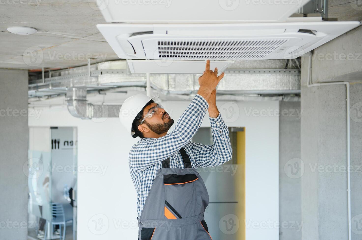 Indian male worker inspecting the air conditioner mounted on the ceiling photo