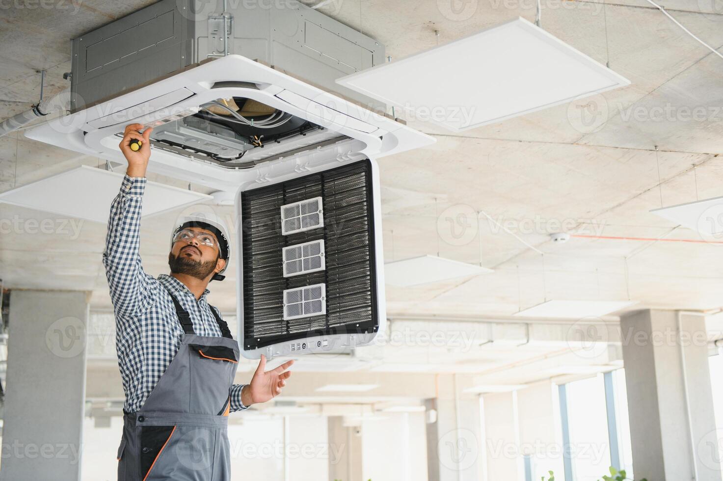 Indian male worker inspecting the air conditioner mounted on the ceiling photo