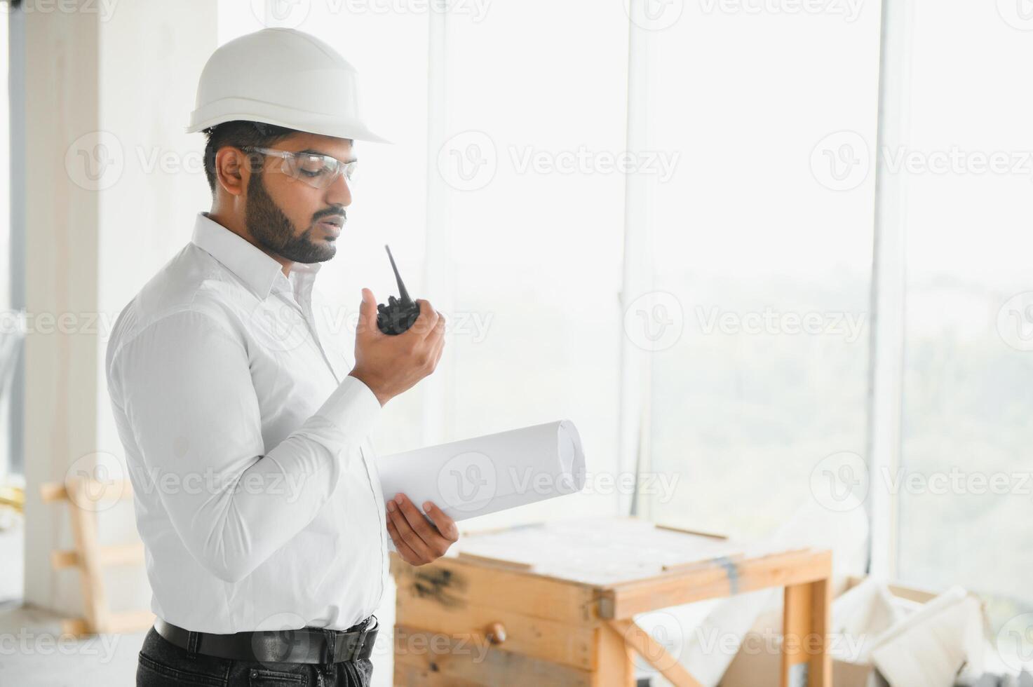 Portrait of young handsome Indian male civil engineer or architect wearing helmet at construction site photo