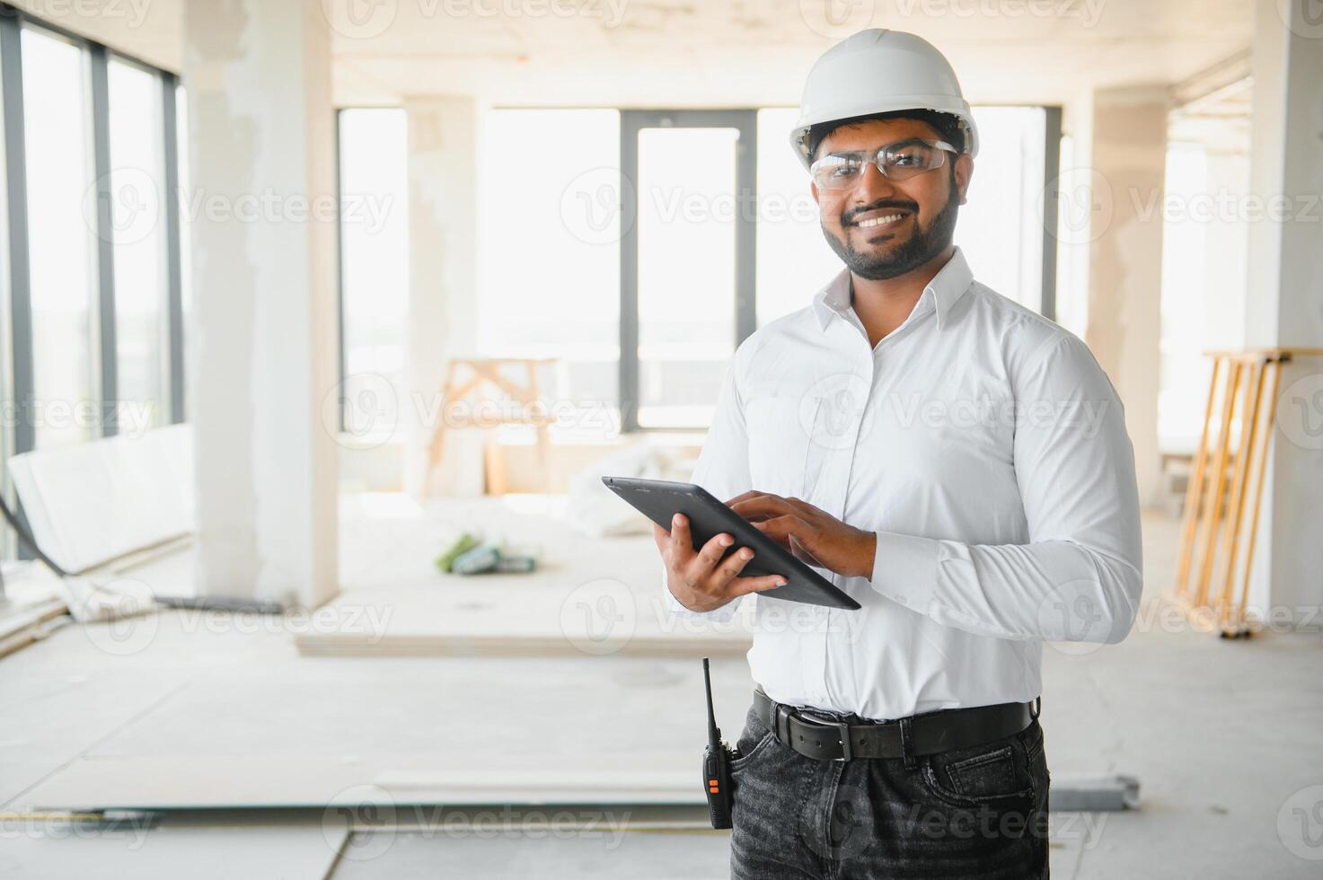 Indian construction site manager standing wearing helmet, thinking at construction site. Portrait of mixed race manual worker or architect photo