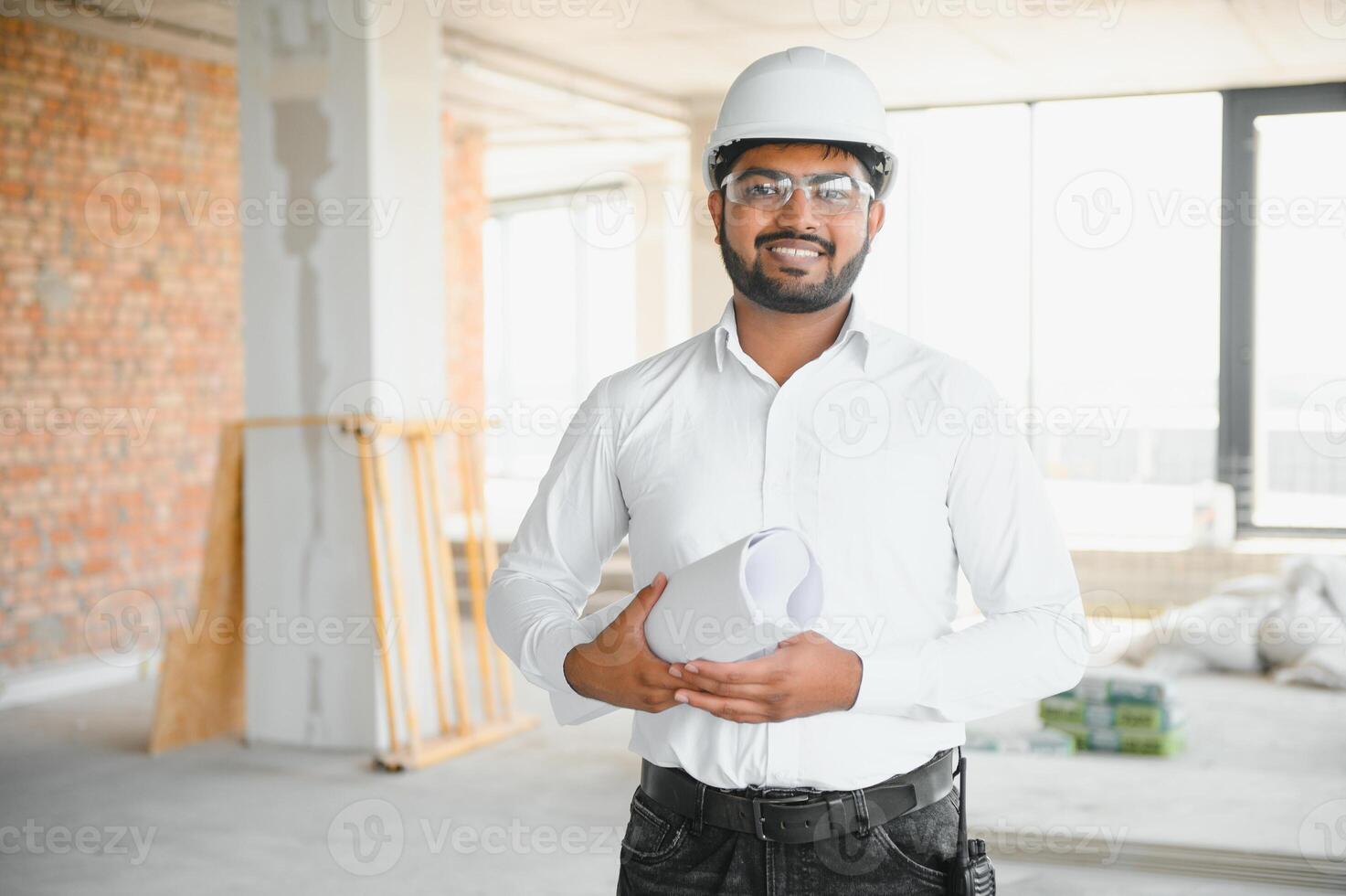 Indian construction site manager standing wearing helmet, thinking at construction site. Portrait of mixed race manual worker or architect photo