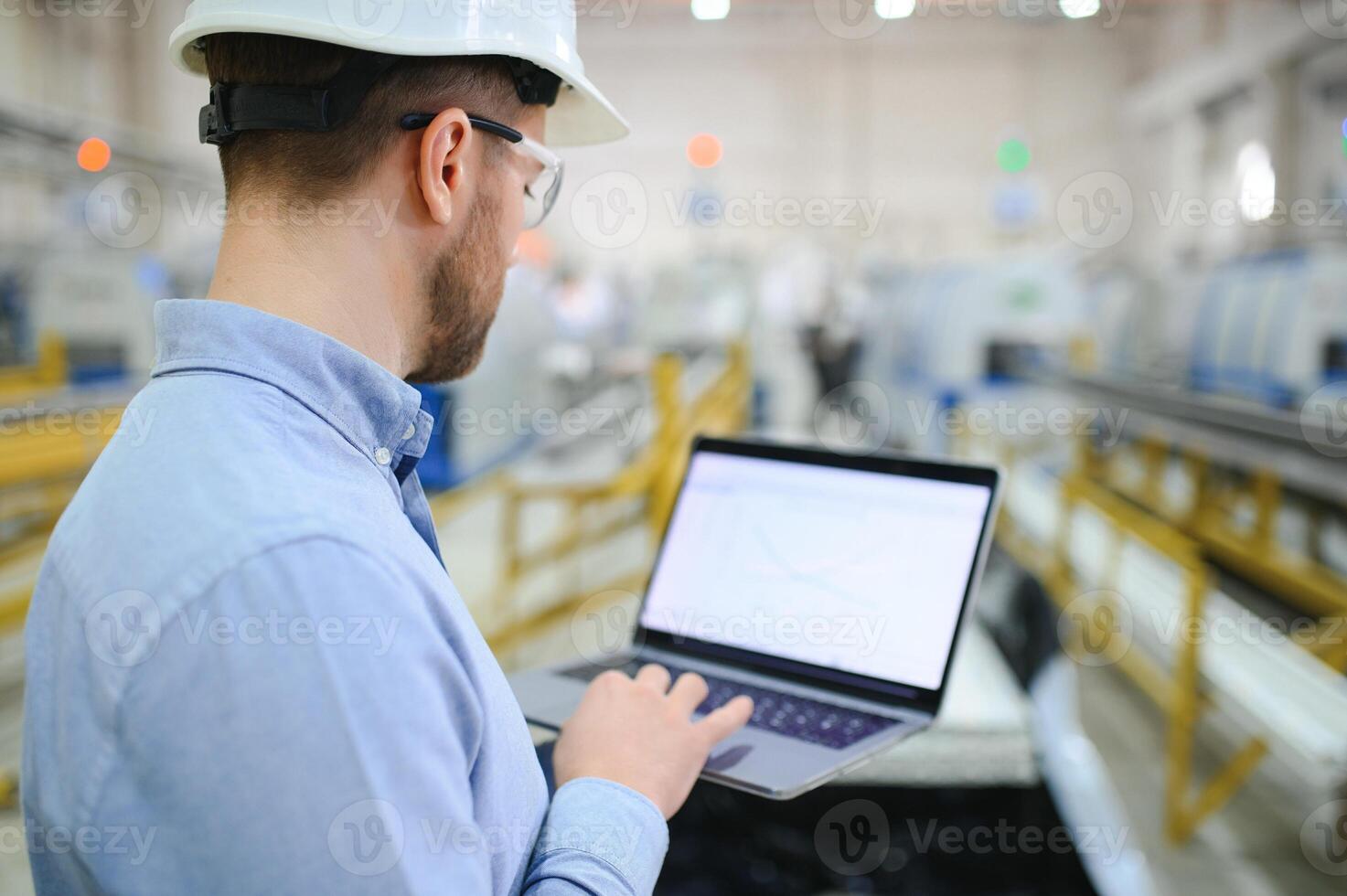 Side view of technician or engineer with headset and laptop standing in industrial factory photo