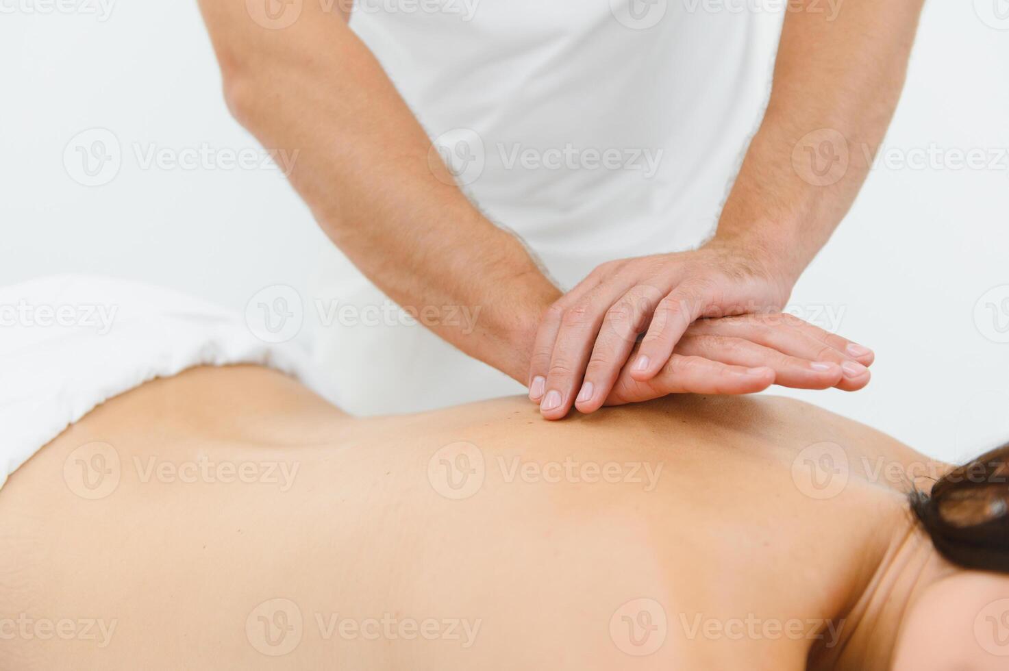 Woman enjoying professional body massage at a modern spa salon. Relaxed young lady lying on a massage table while a skilled masseur is gently massaging her back. Beauty, health, pleasure, concept photo