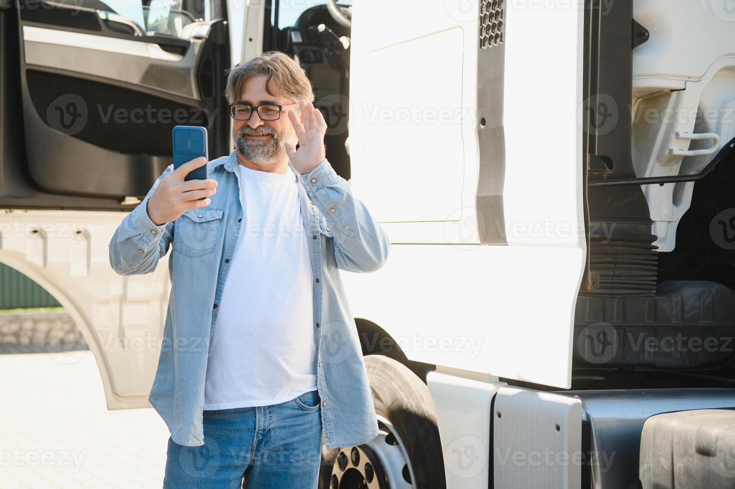 Truck driver standing by his truck and talking on the phone. Man driver getting in touch with his family photo