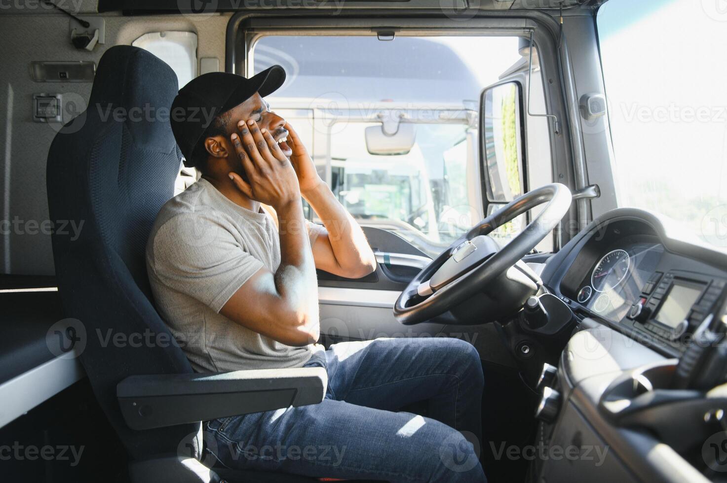 Tired of work. Sitting in the cabin. Young african american truck driver is with his vehicle at daytime photo