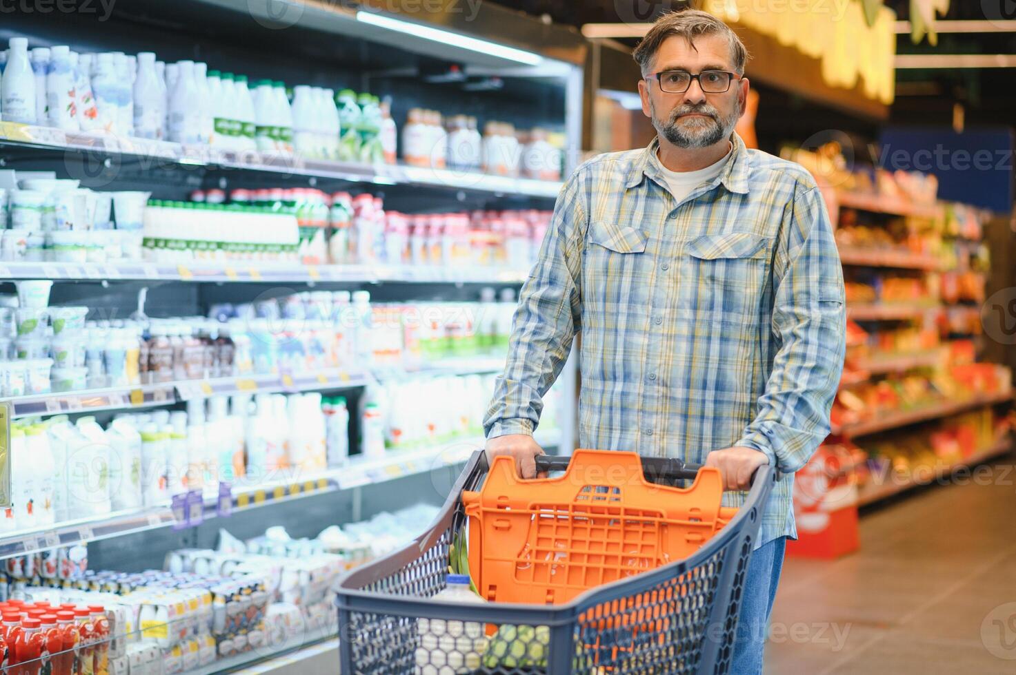 Mature man pushing a shopping cart at the supermarket, he is buying groceries, grocery shopping concept photo