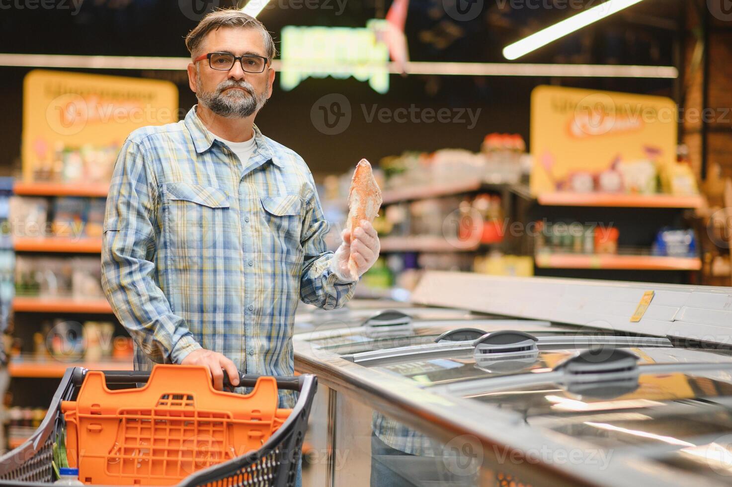 Bearded man with frozen fish his hands stands at the refrigerator in the department of frozen food photo