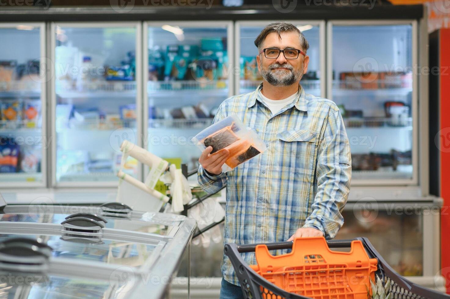 Mature man pushing a shopping cart at the supermarket, he is buying groceries, grocery shopping concept photo