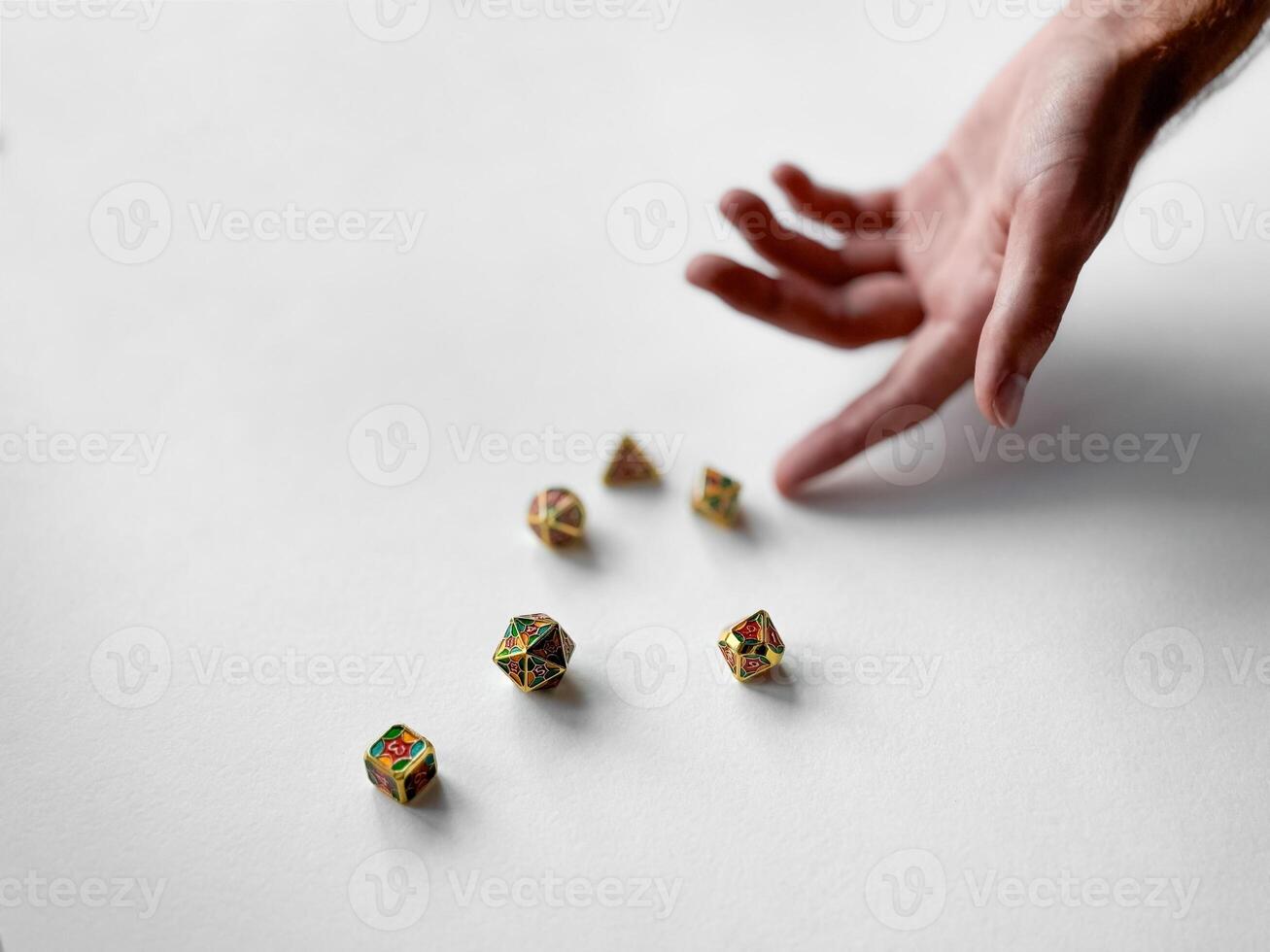 Hand reaching for colorful polyhedral dice on white surface photo