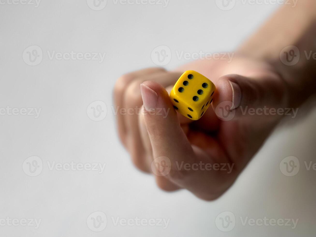 Close-up of hand holding yellow dice with black dots on minimalist background photo