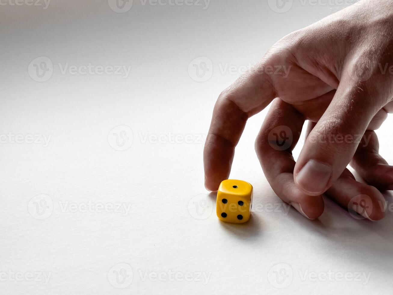 Hand rolling yellow dice on white surface for luck and strategy photo