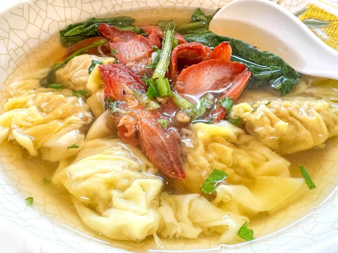 Closeup Chinese food Dumplings in pork bone soup with roasted red pork in white ceramic bowl. photo