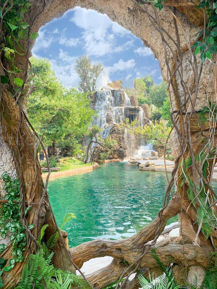 Closeup view of a beautiful waterfall and bright blue sky with clouds through holes in trees and then vines. photo